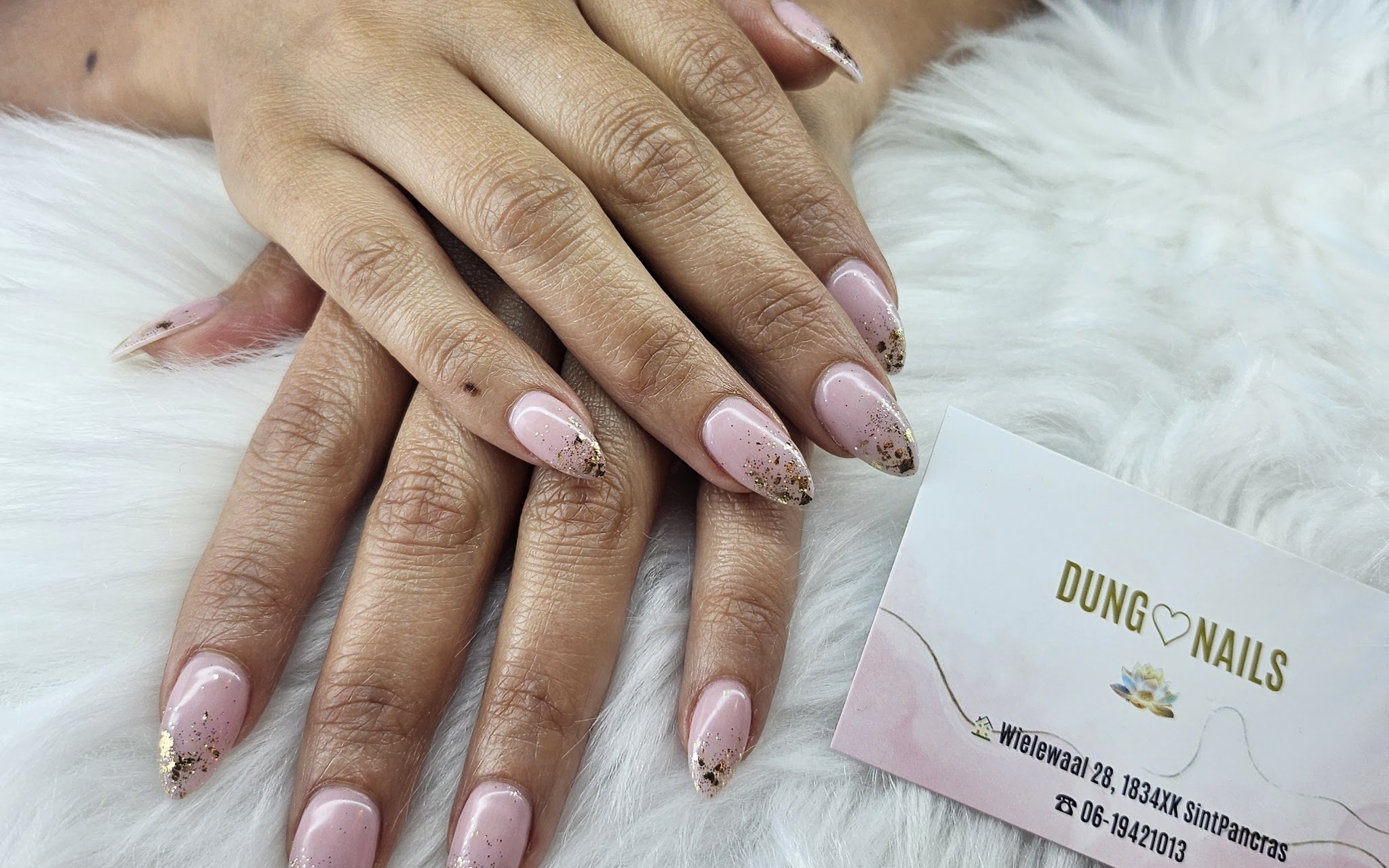 Amandelvormige roze nagels met goudfolie, naast het visitekaartje van Dung nails