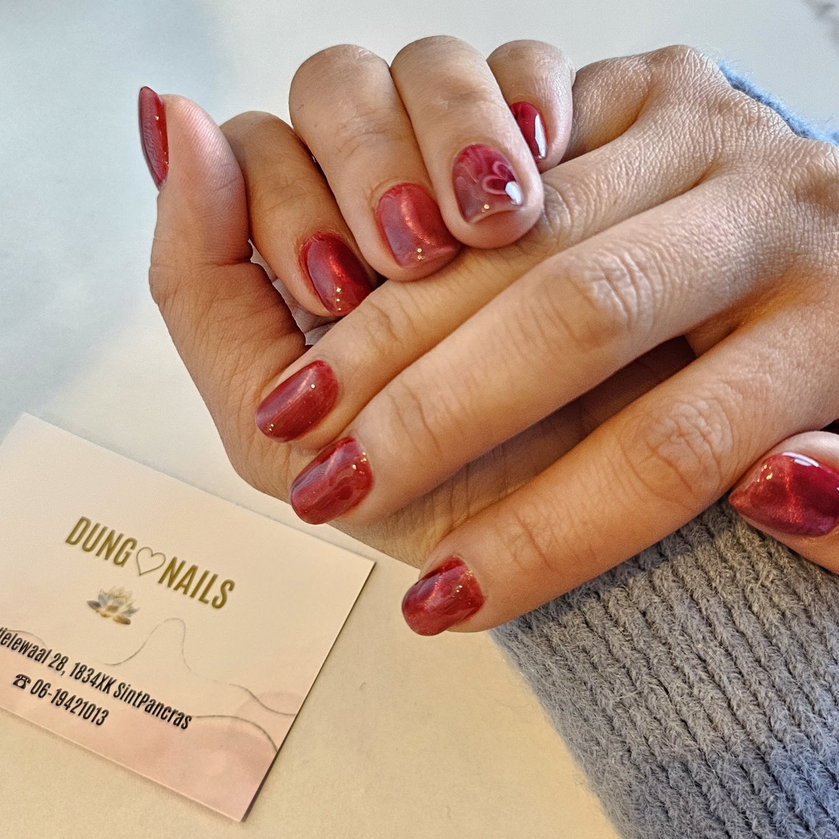 Korte gemarmerde rode nagels naast het visitekaartje van Dung nails